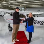 A man and woman shaking hands in front of an airplane