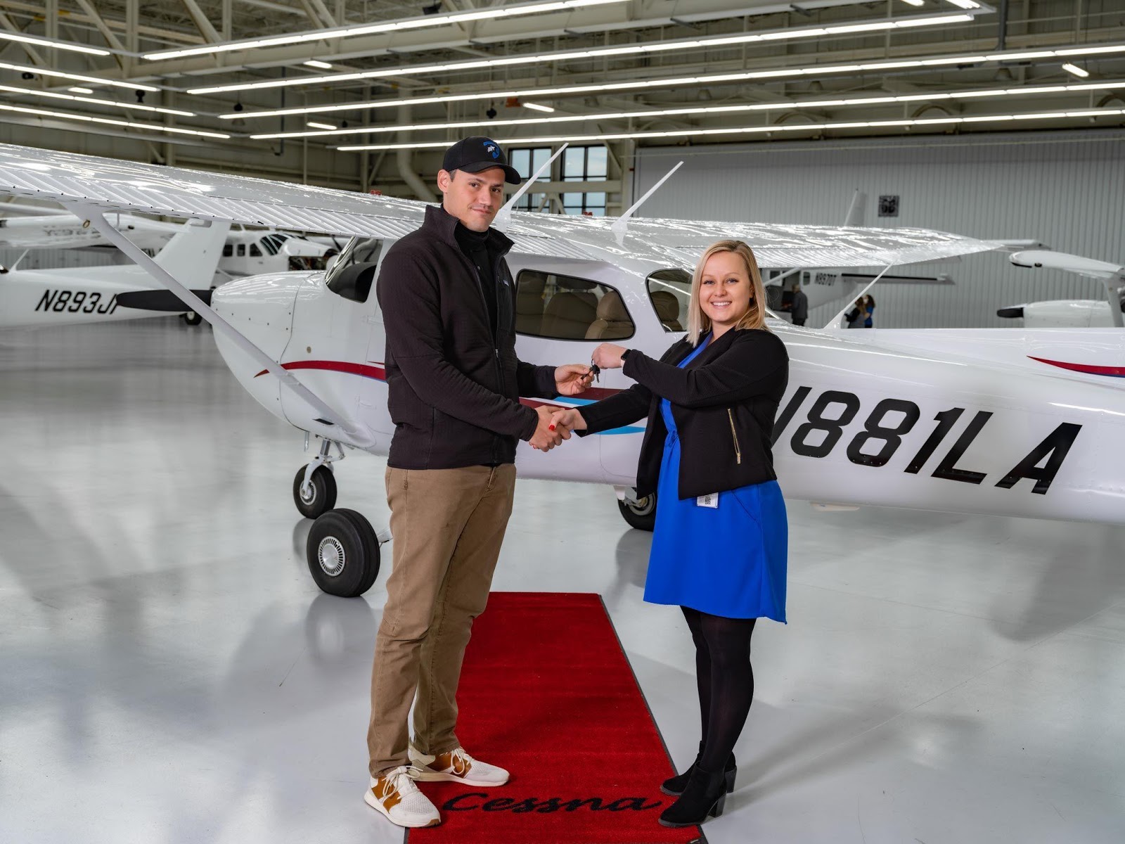 A man and woman shaking hands in front of an airplane